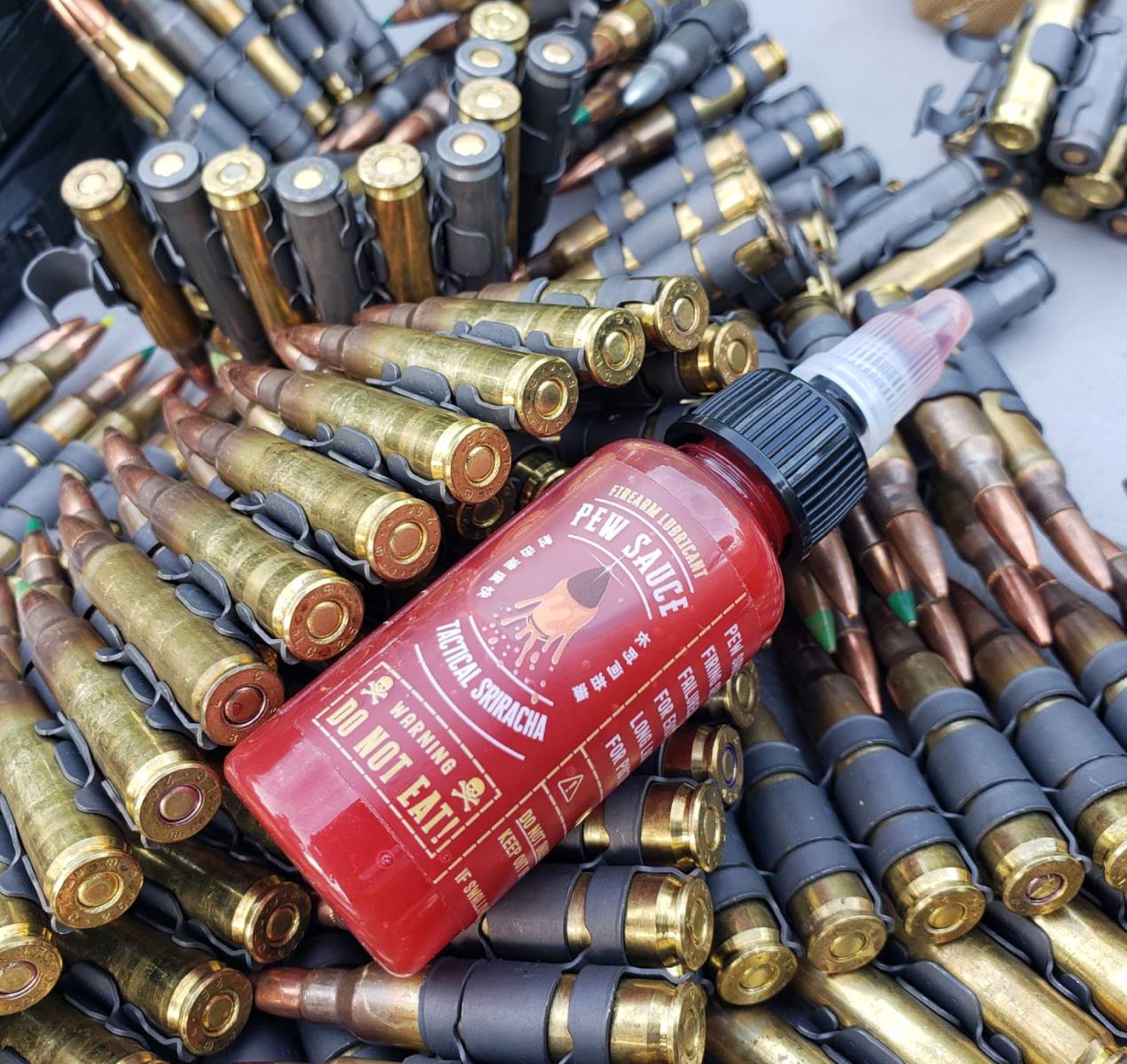 Pew Sauce bottle laid across a belt of linked rifle ammunition
