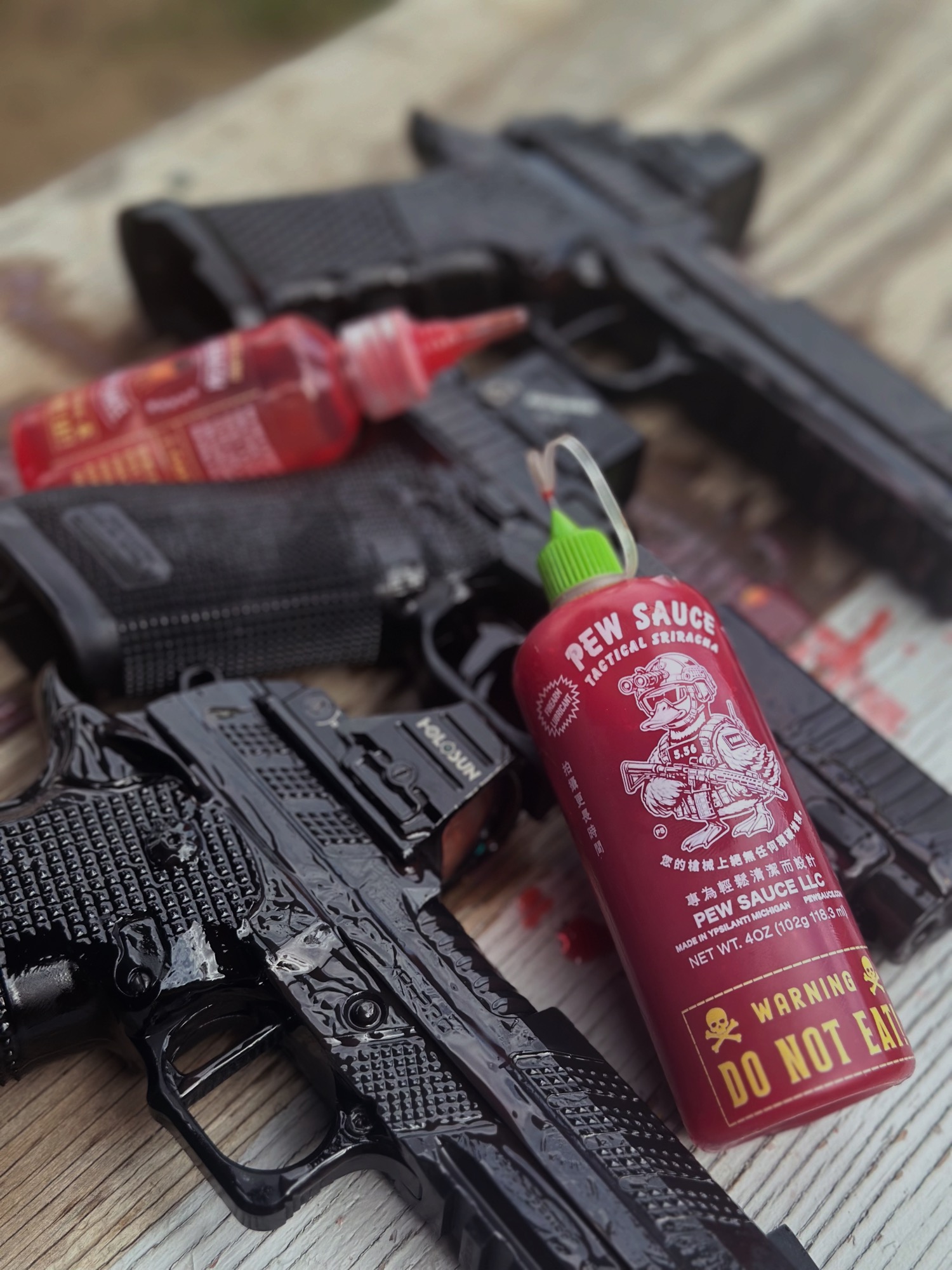 Pew Sauce Tactical Sriracha bottle propped between two pistols on a range bench
