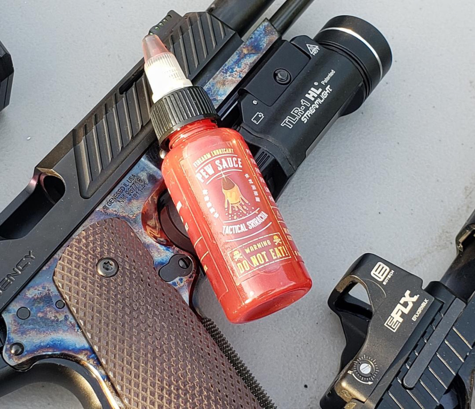 Pew Sauce bottle resting on a case-hardened 1911 with Streamlight mounted