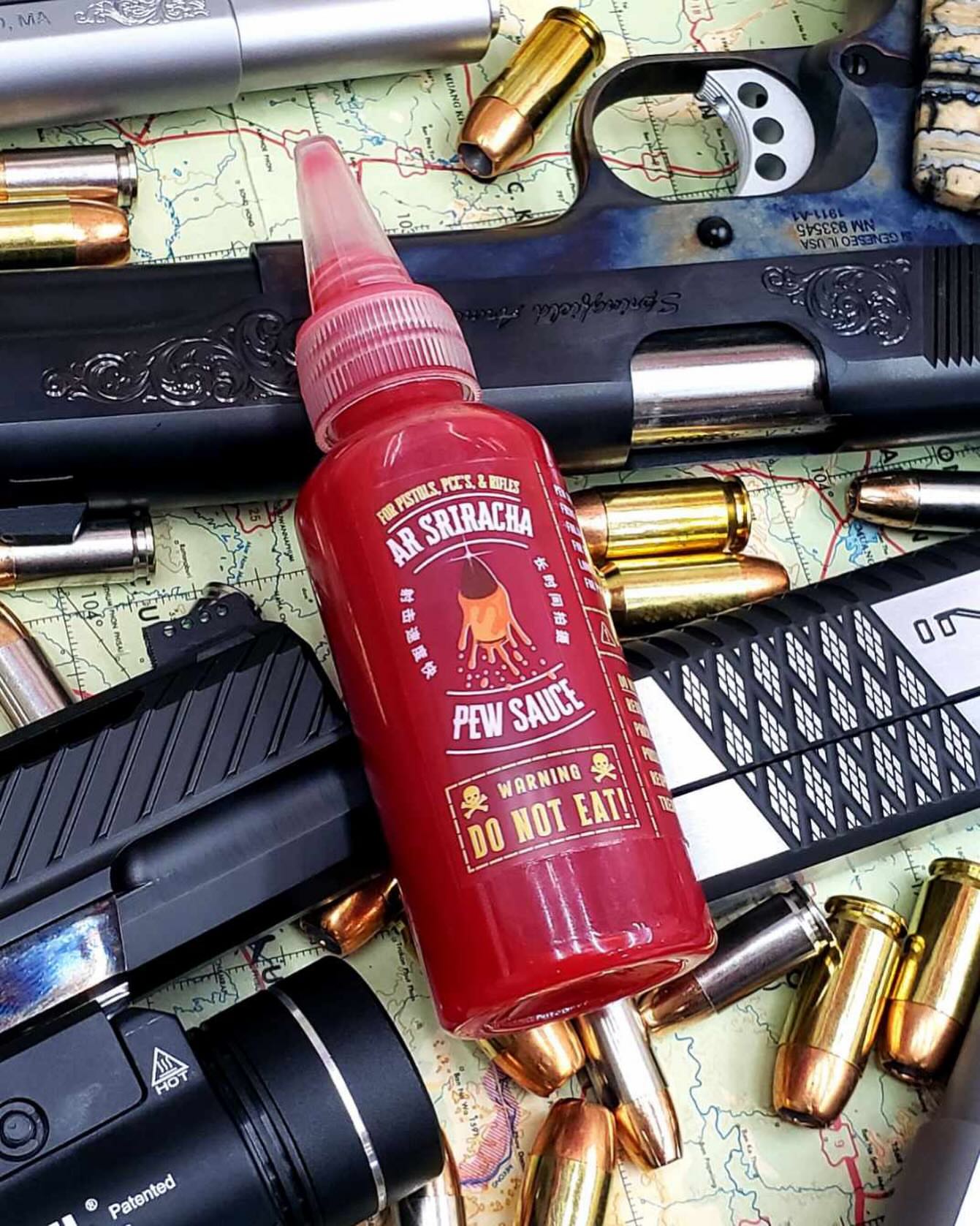 Pew Sauce Tactical Sriracha bottle on a tactical map surrounded by pistols and ammunition